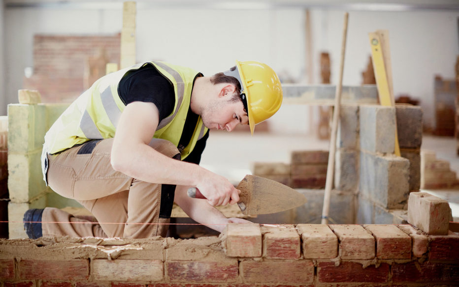 A student at Sunderland College, wearing a hi-vis jacket and hardhat, and working on bricklaying