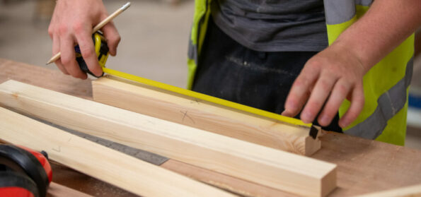 An image of a student at Northumberland College Ashington Campus, measuring a plank of wood with a tape measure
